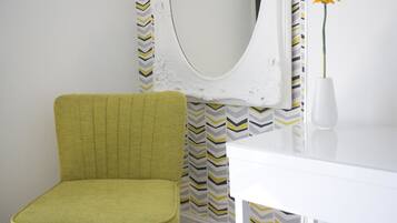 A room with a green chair, a white table, and a mirror with a chevron-patterned curtain.