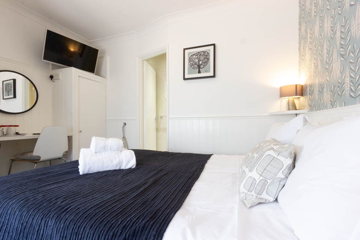 A hotel room with a bed, a desk with a chair, a TV mounted on the wall, and a framed picture.