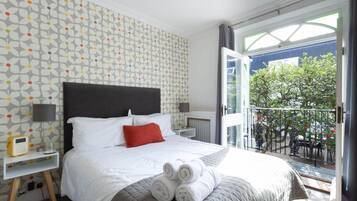 A hotel room with a bed, a nightstand, a balcony with a view of trees and a railing.