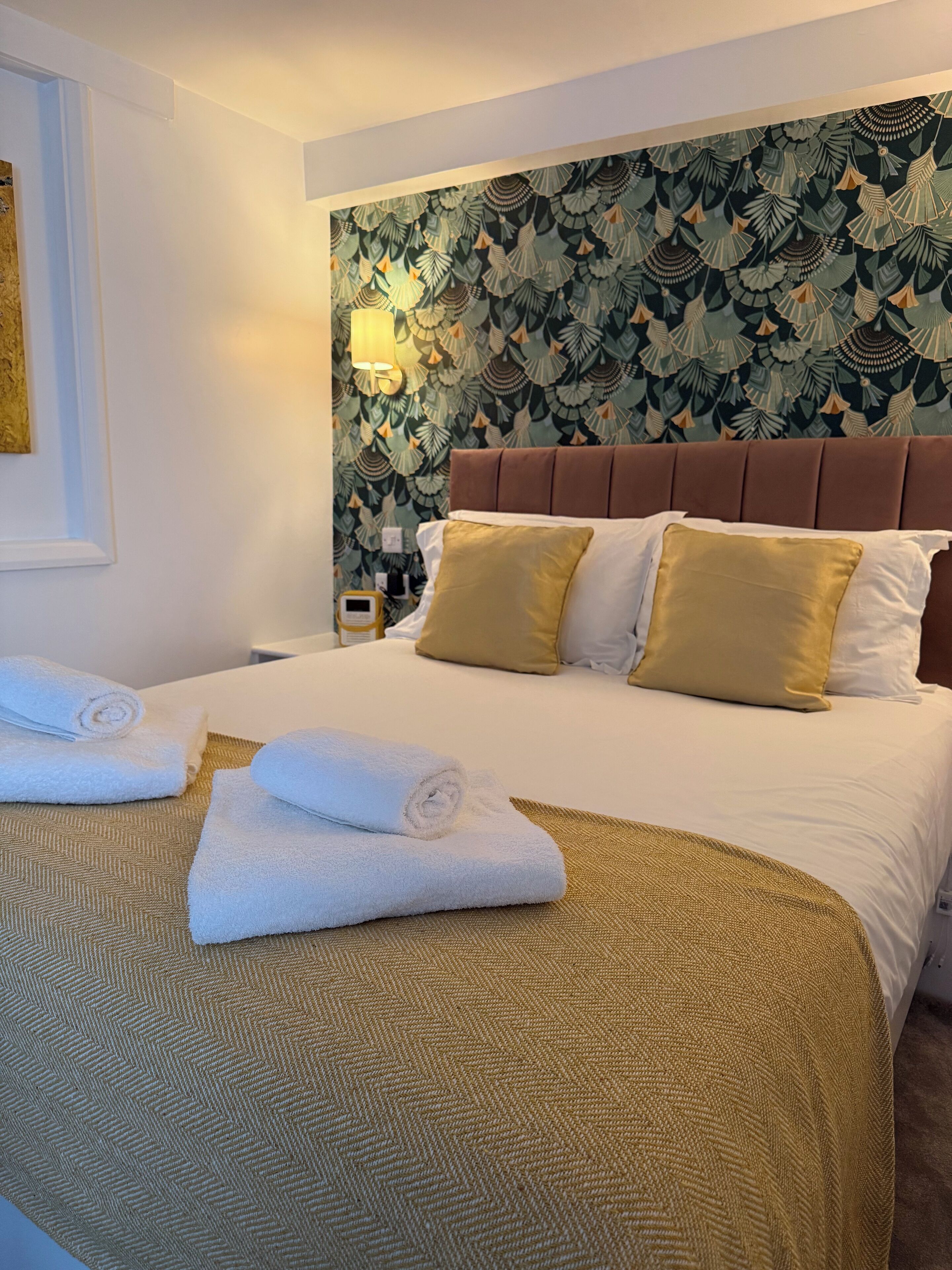 A hotel room with a large bed, a patterned wallpaper, and a wall-mounted lamp.