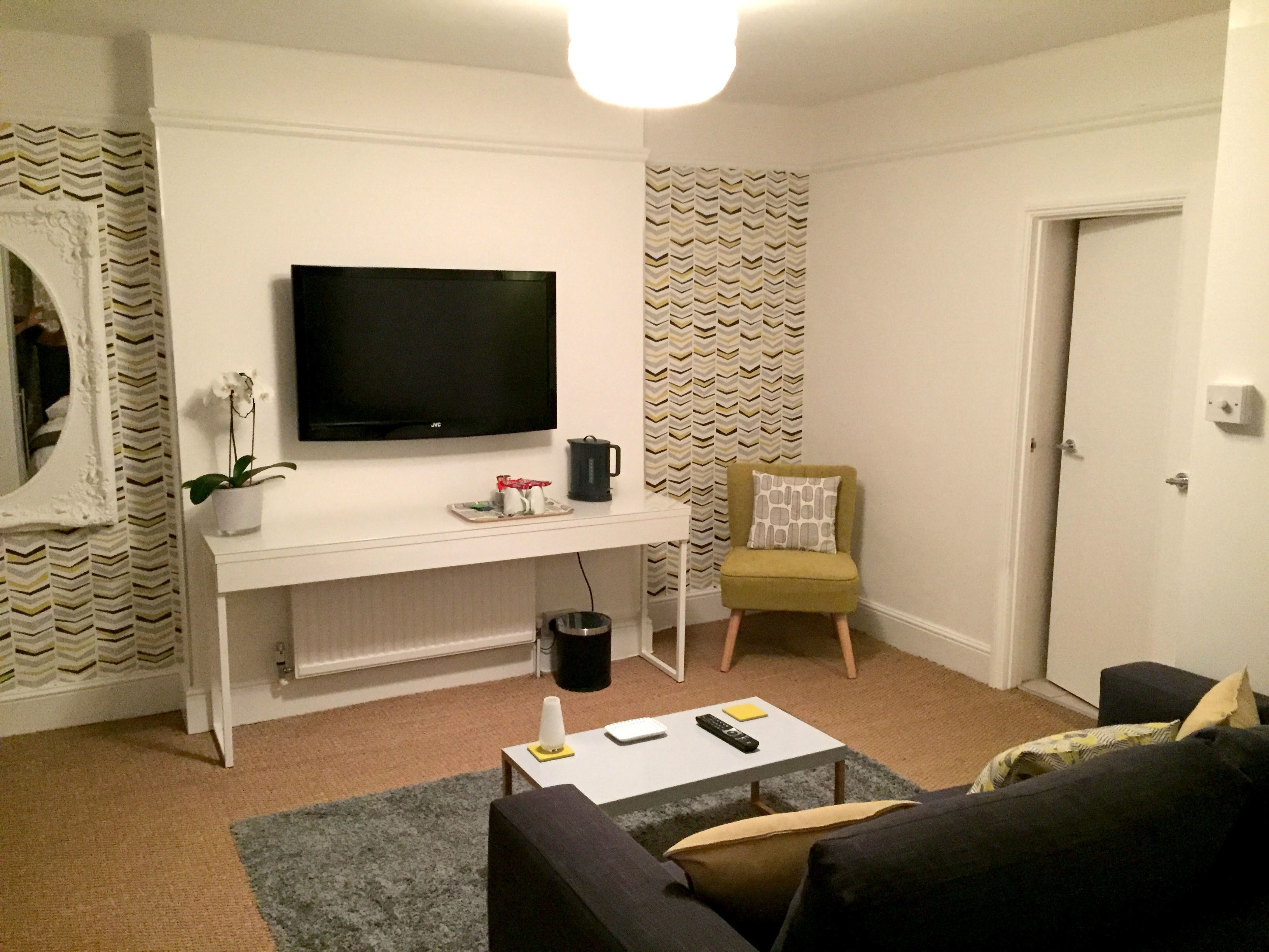 A living room with a flat-screen TV, a coffee table, a sofa, a chair, and a door.