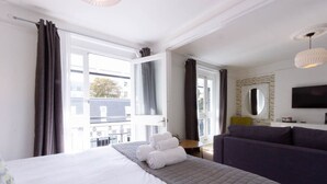 A hotel room with a large bed, a sofa, a TV, and a balcony with curtains. - The White House (Brighton)