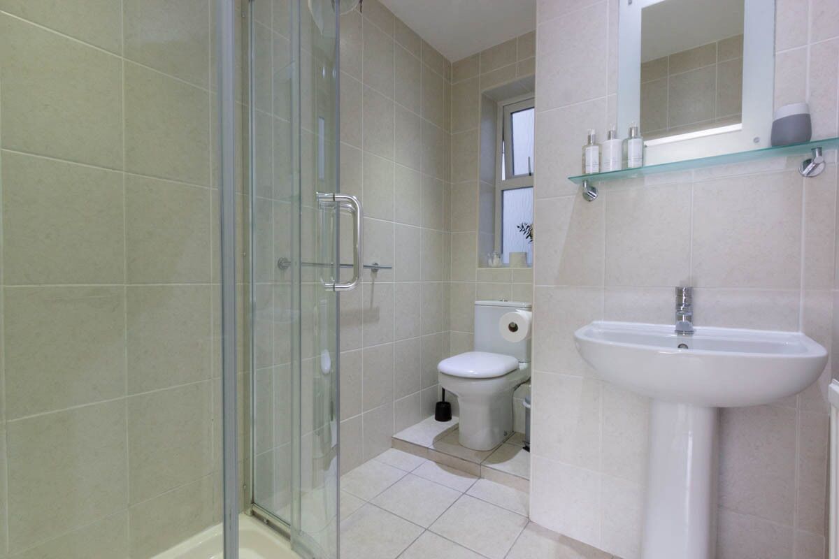 Un baño con cabina de ducha de vidrio, inodoro y lavamanos pedestal.