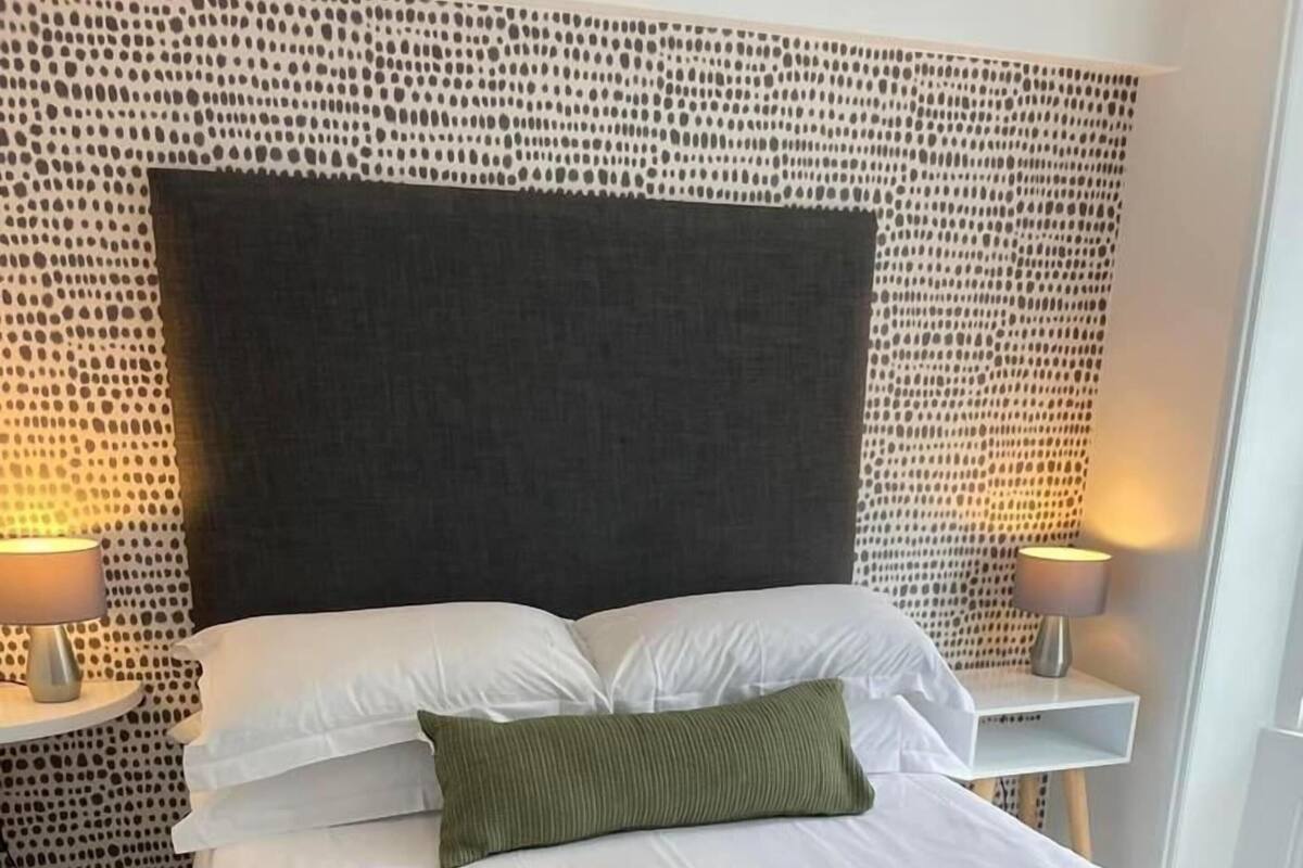 A neatly made bed with white linens, a green throw, and two folded towels.