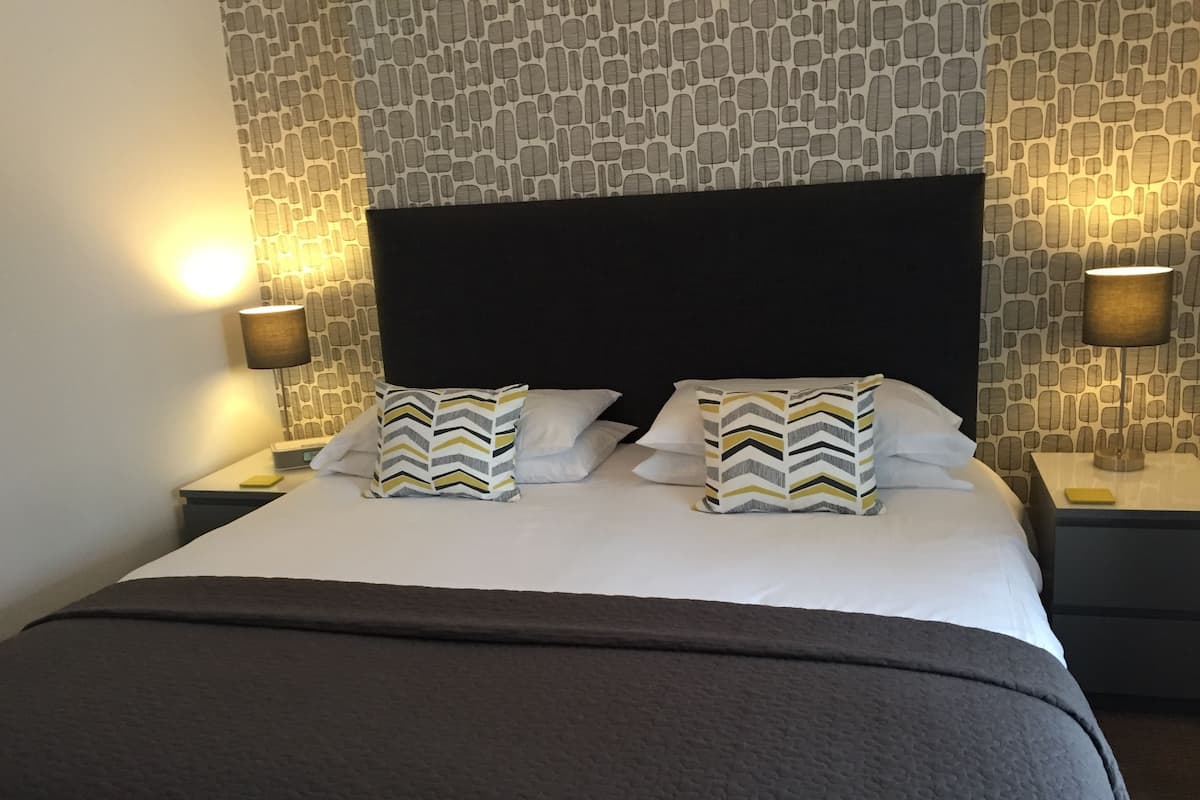 A neatly made bed with two decorative pillows, a black headboard, and a patterned wall.