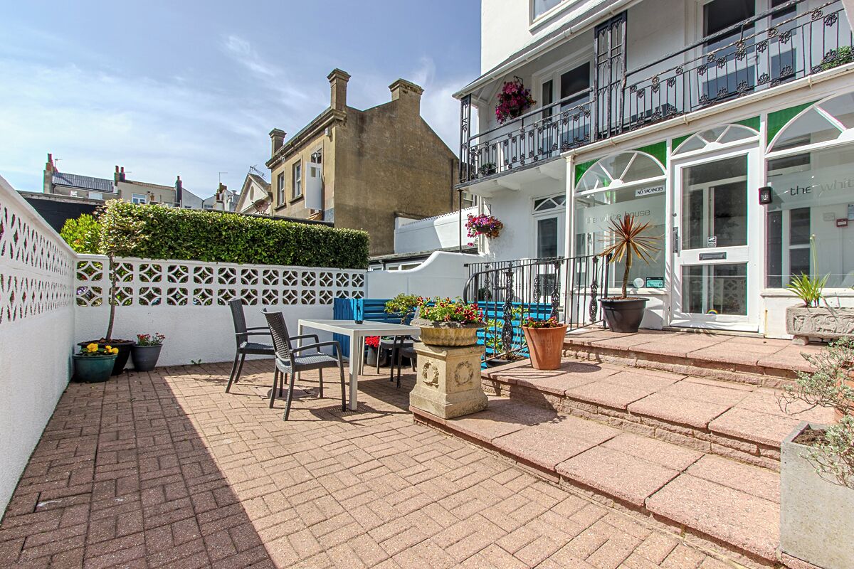 A courtyard with a table and chairs, potted plants, and a white fence.