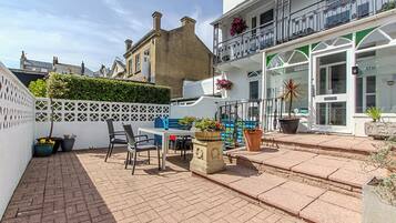 A courtyard with a table and chairs, potted plants, and a white fence.