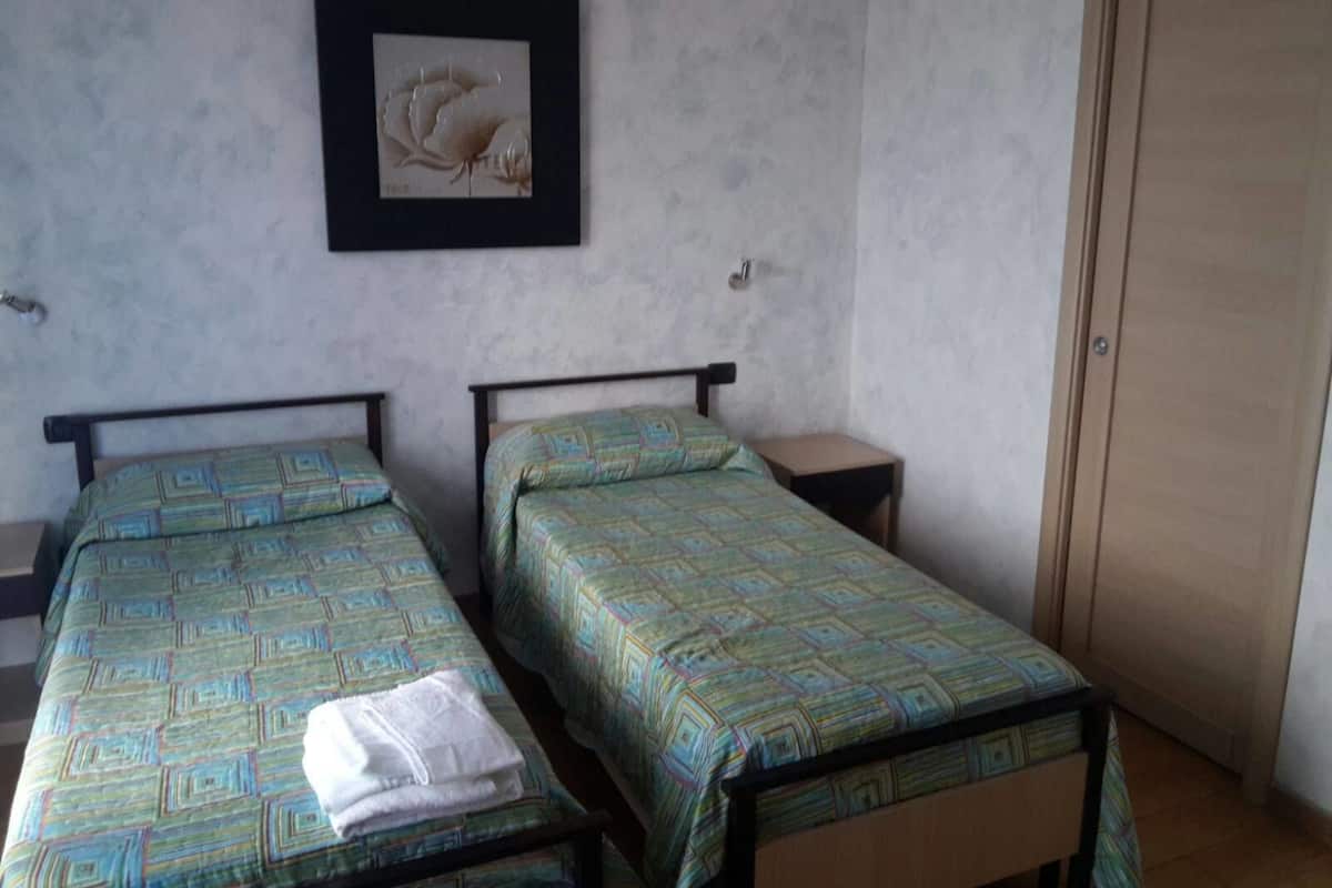 Una habitación con dos camas individuales, una mesita de noche pequeña, un cuadro en la pared y una puerta de madera.