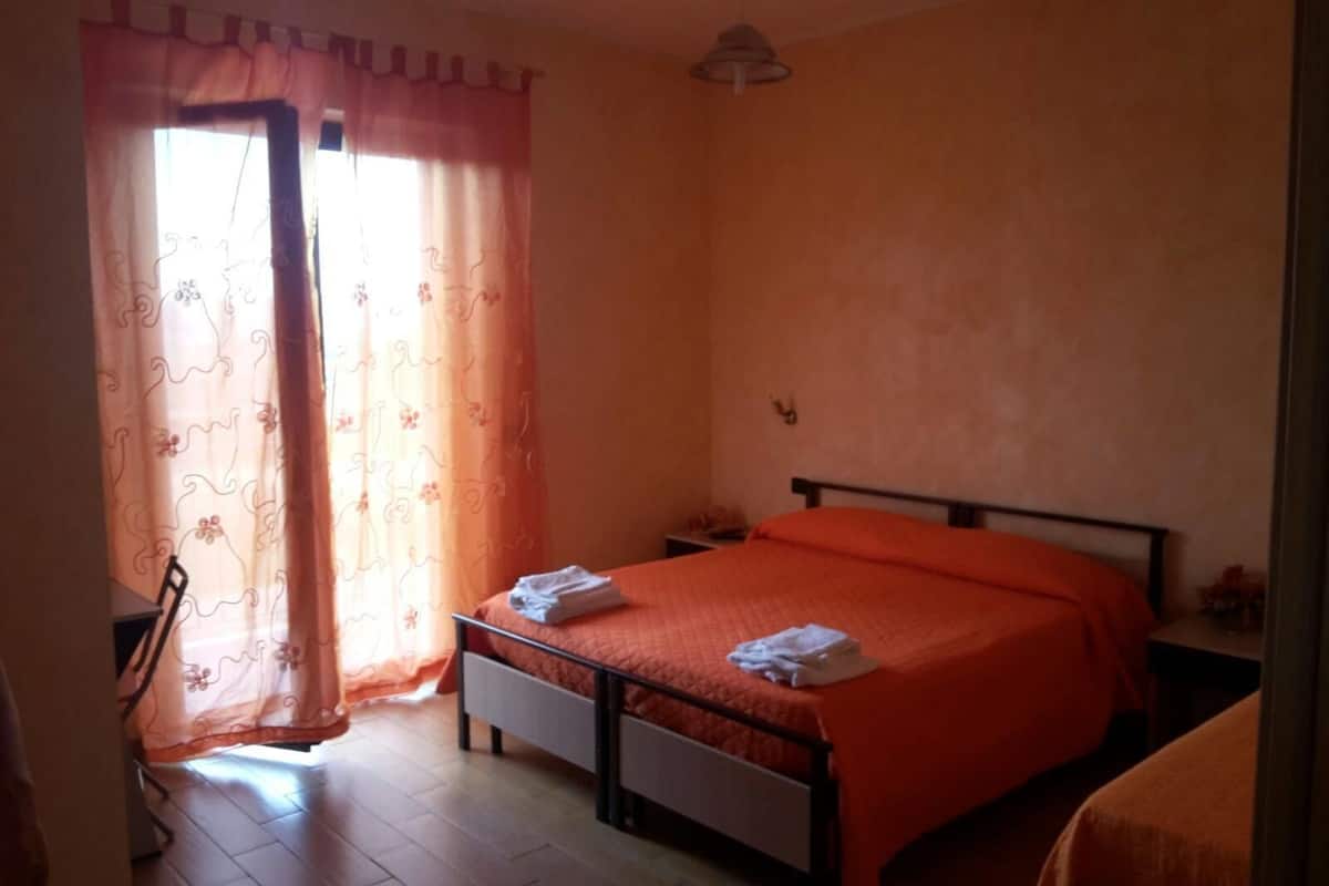 Un dormitorio con cama, mesita de noche, lámpara y ventana con cortinas.