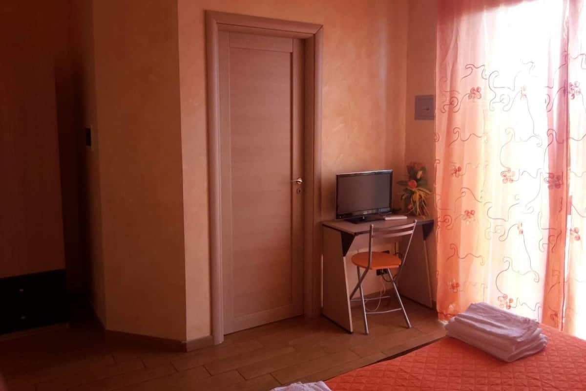 Una habitación pequeña con una cama, un escritorio con una computadora, una silla y una puerta.