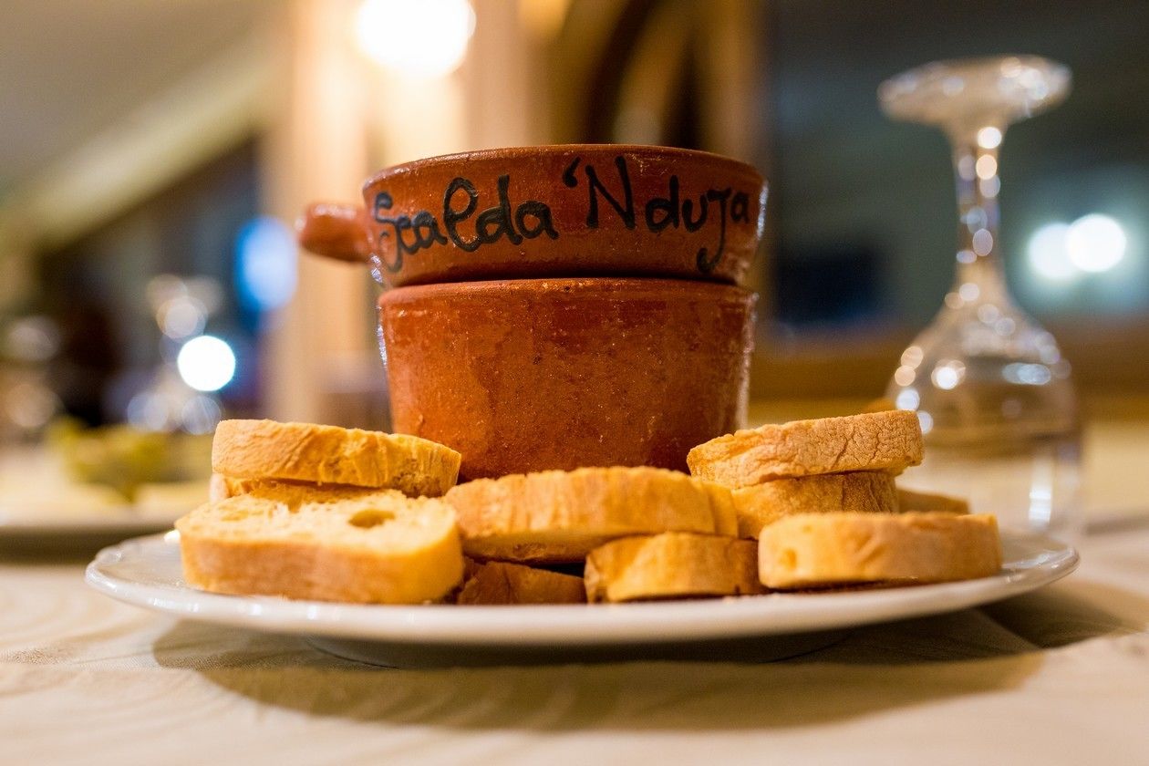 A clay cup with 'Scalda' written on it, accompanied by several pieces of bread on a plate.