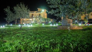 Un espacio exterior bien iluminado con una estatua, un edificio con ventanas iluminadas y un primer plano con césped.