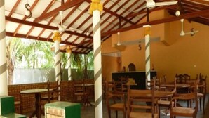 An indoor dining area with wooden tables and chairs, a high ceiling with exposed beams, and a view of greenery outside. - Regina Holiday Home (Thissamaharama)