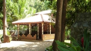 A small, single-story structure with a tiled roof, surrounded by lush greenery and trees. - Regina Holiday Home (Thissamaharama)