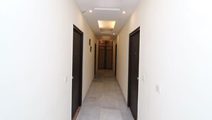 A narrow hallway with a tiled floor, two doors on each side, and a wooden door at the end. - OYO 27718 Viva Destinations (Gurugram)