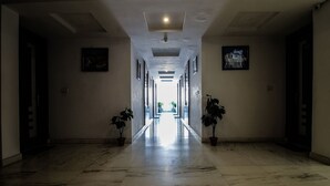 A long, well-lit hallway with marble flooring, flanked by potted plants and framed artwork on the walls. - OYO 25125 Paharganj Dx (New Delhi)