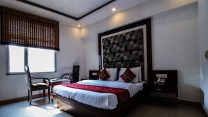 A hotel room with a large bed, a desk with a chair, a window with blinds, and a ceiling fan. - OYO 25125 Paharganj Dx (New Delhi)