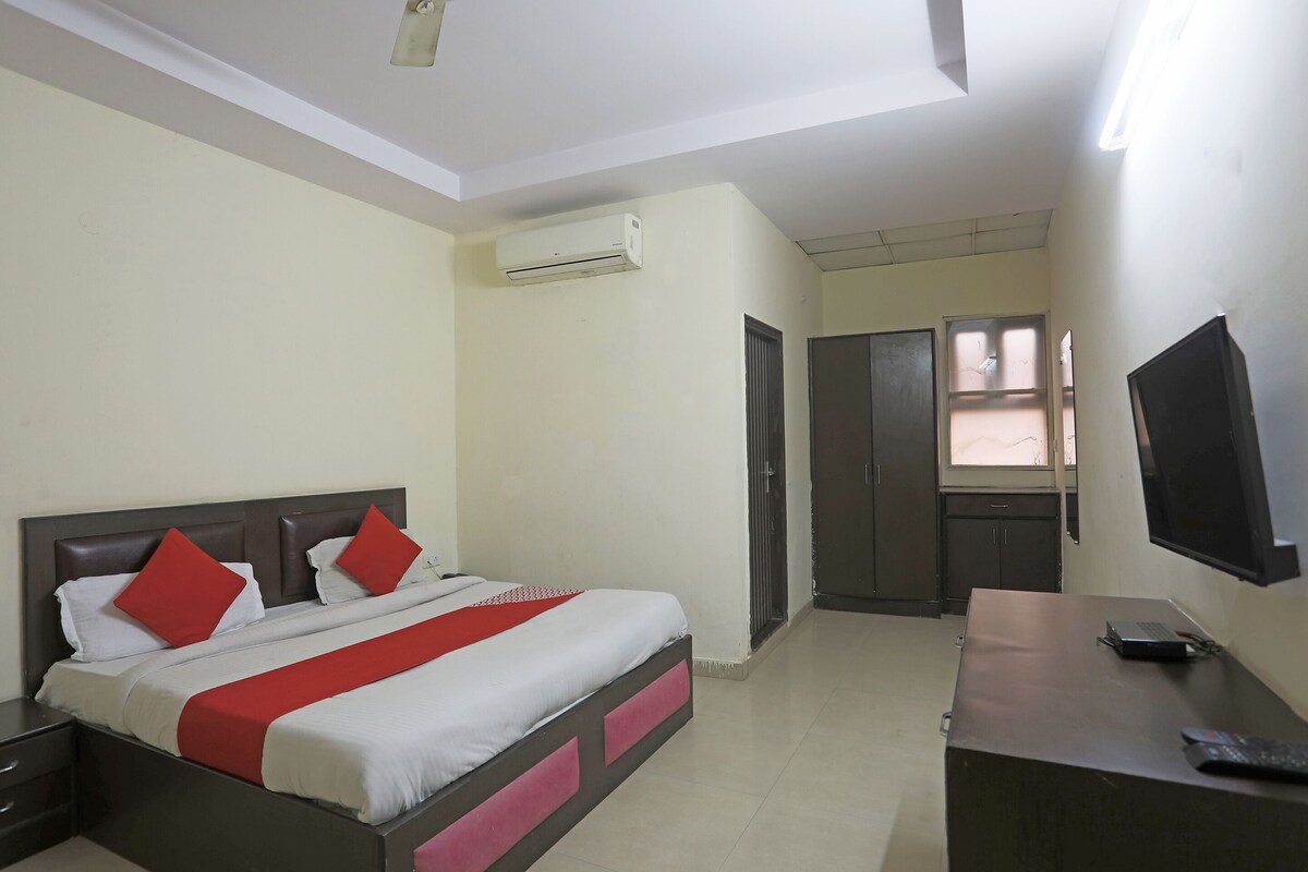 A hotel room with a bed, a desk, a TV, and an air conditioning unit.