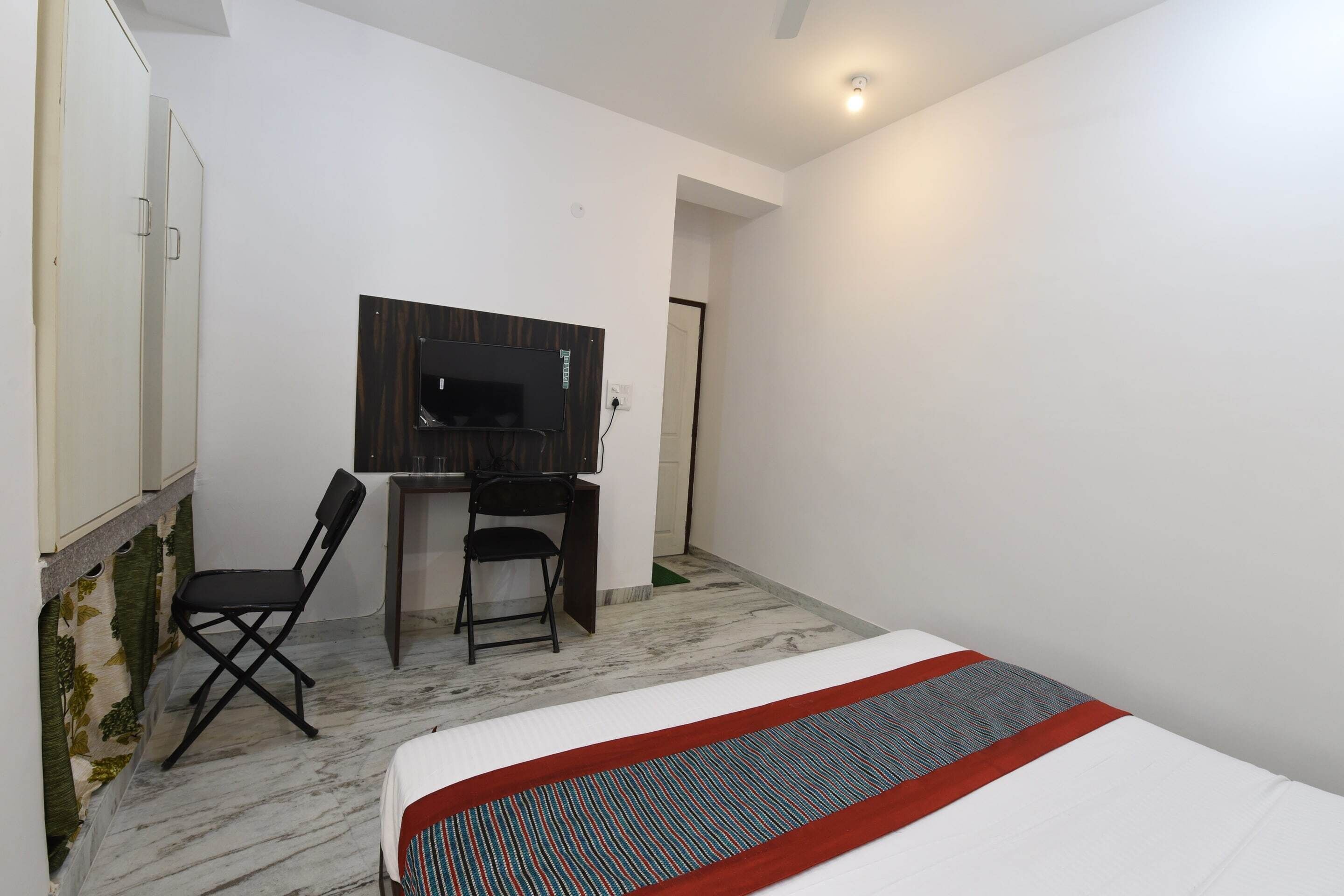 A hotel room with a bed, a desk with a chair, a television, and a wardrobe.