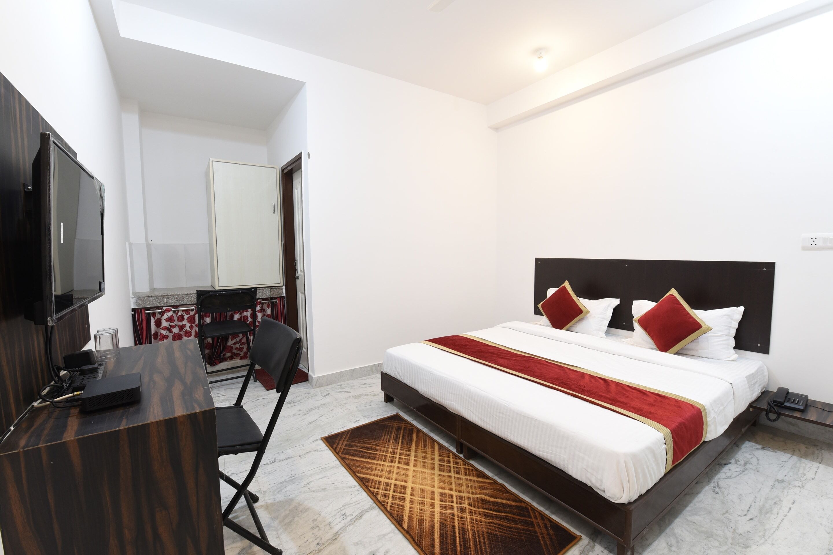 A hotel room with a bed, a desk, a chair, a television, and a bathroom visible in the background.