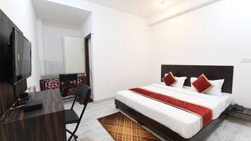 A hotel room with a bed, a desk, a chair, a television, and a bathroom visible in the background.