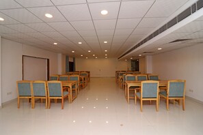 A conference room with rows of wooden chairs and tables, a tiled floor, and a ceiling with recessed lighting. - OYO 26911 Kcg Hotels (New Delhi)