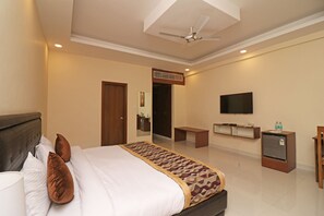 A hotel room with a bed, a desk, a television, and a minibar. - OYO 26911 Kcg Hotels (New Delhi)