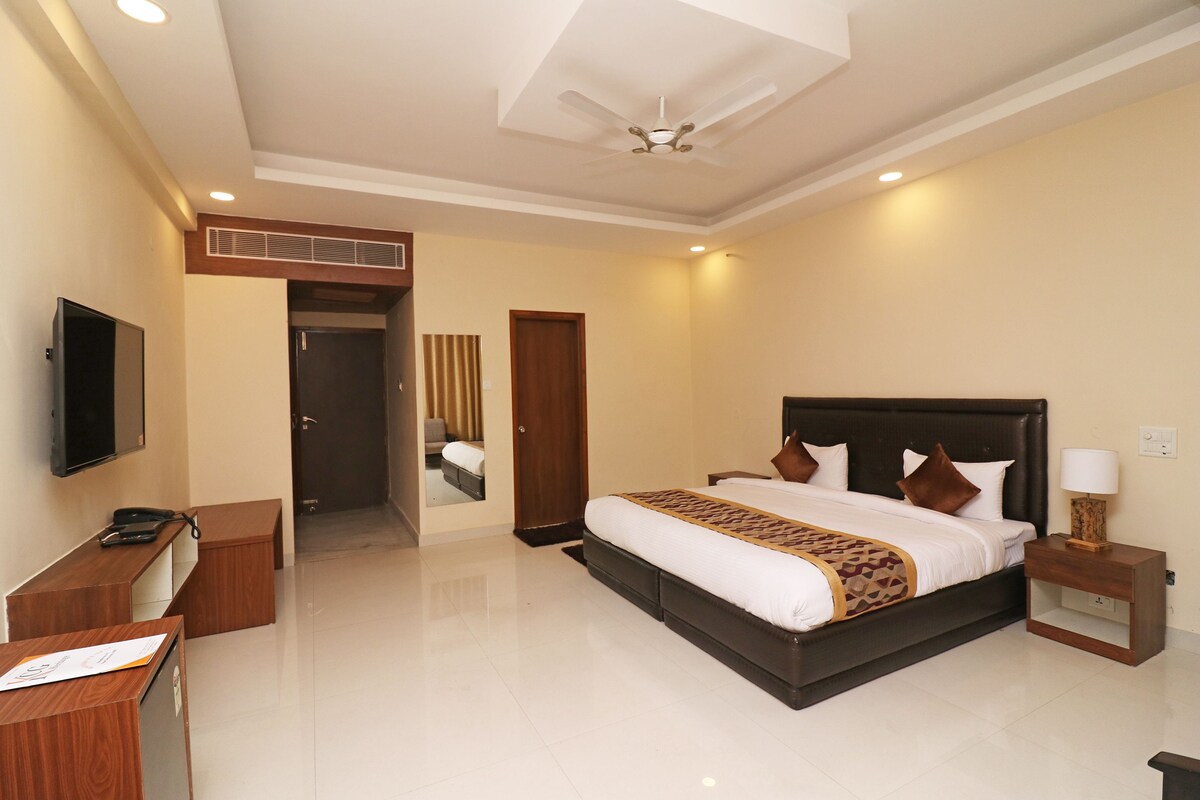 A hotel room with a large bed, a desk with a telephone, a bedside table with a lamp, and a ceiling fan.