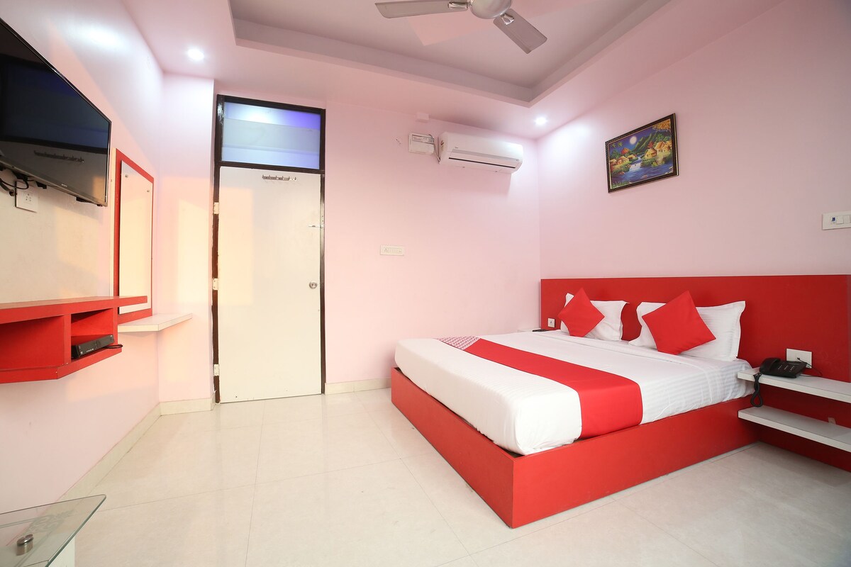A bedroom with a red and white bed, a TV, a ceiling fan, and an air conditioning unit.