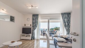 A modern living room with a flat-screen TV, a dining area with a table set for two, and a balcony with outdoor seating. - Apartments with Pool Villa Zora (Novalja)