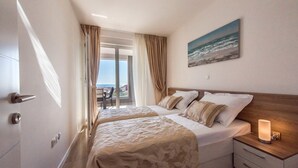 A hotel room with two beds, a nightstand with a lamp, a painting of the ocean, and a view of the sea through the window. - Apartments with Pool Villa Zora (Novalja)