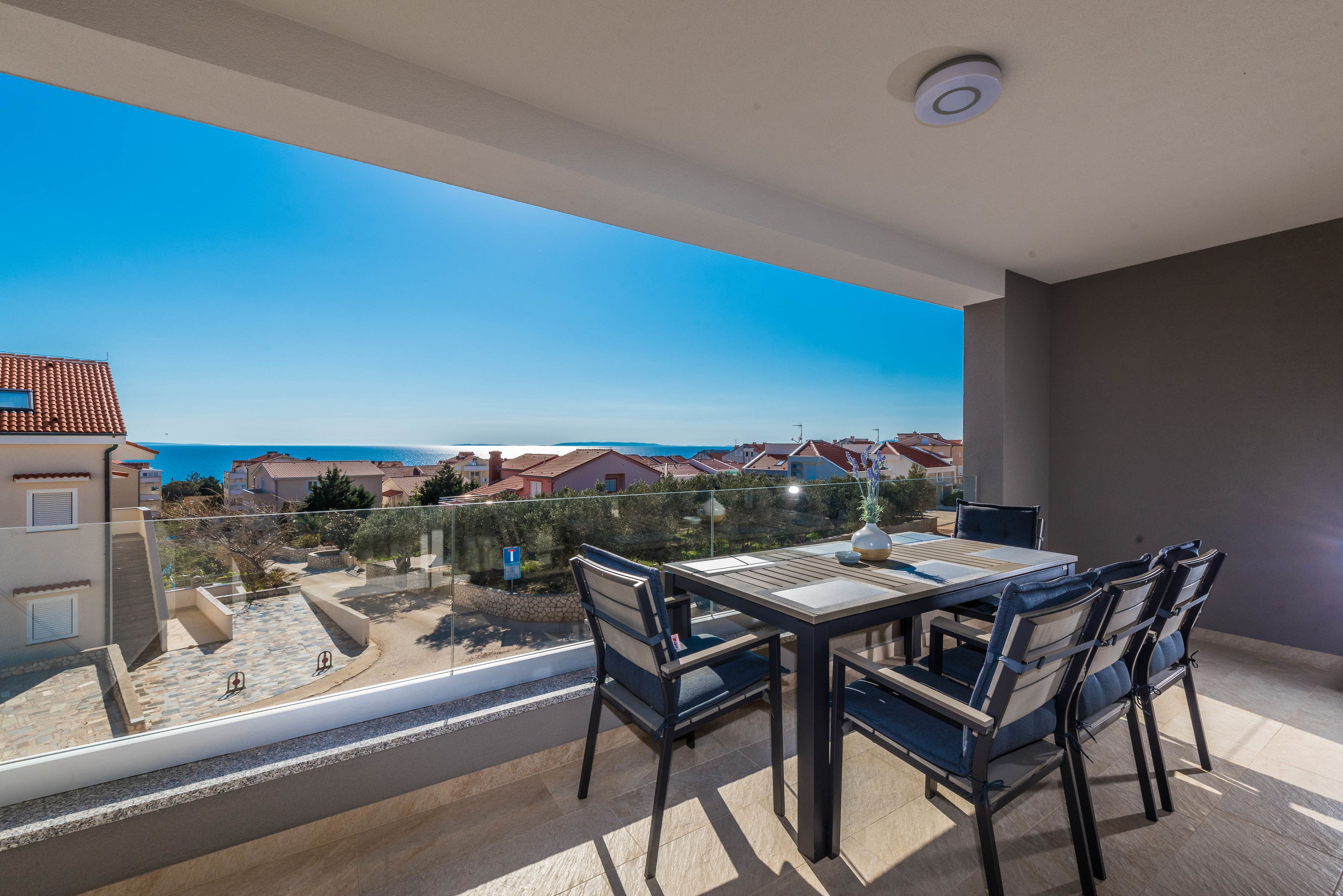 A balcony with a table and chairs, overlooking a residential area and the sea.