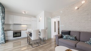 A modern living room with a grey sofa, a white coffee table, and a dining area with white chairs and a glass-top table. - Apartments with Pool Villa Zora (Novalja)