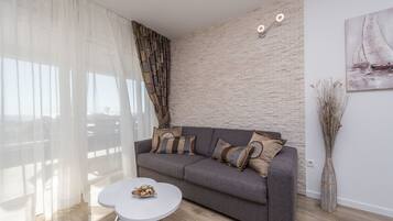Ein modernes Wohnzimmer mit einem grauen Sofa, weißen Vorhängen, einem weißen Couchtisch und einer Ziegelwand.