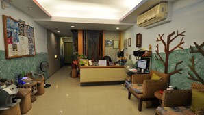 A reception area with a reception desk, seating area with wicker furniture, a bulletin board, and an air conditioning unit. - Tz Shin Resort Hostel (Hengchun)
