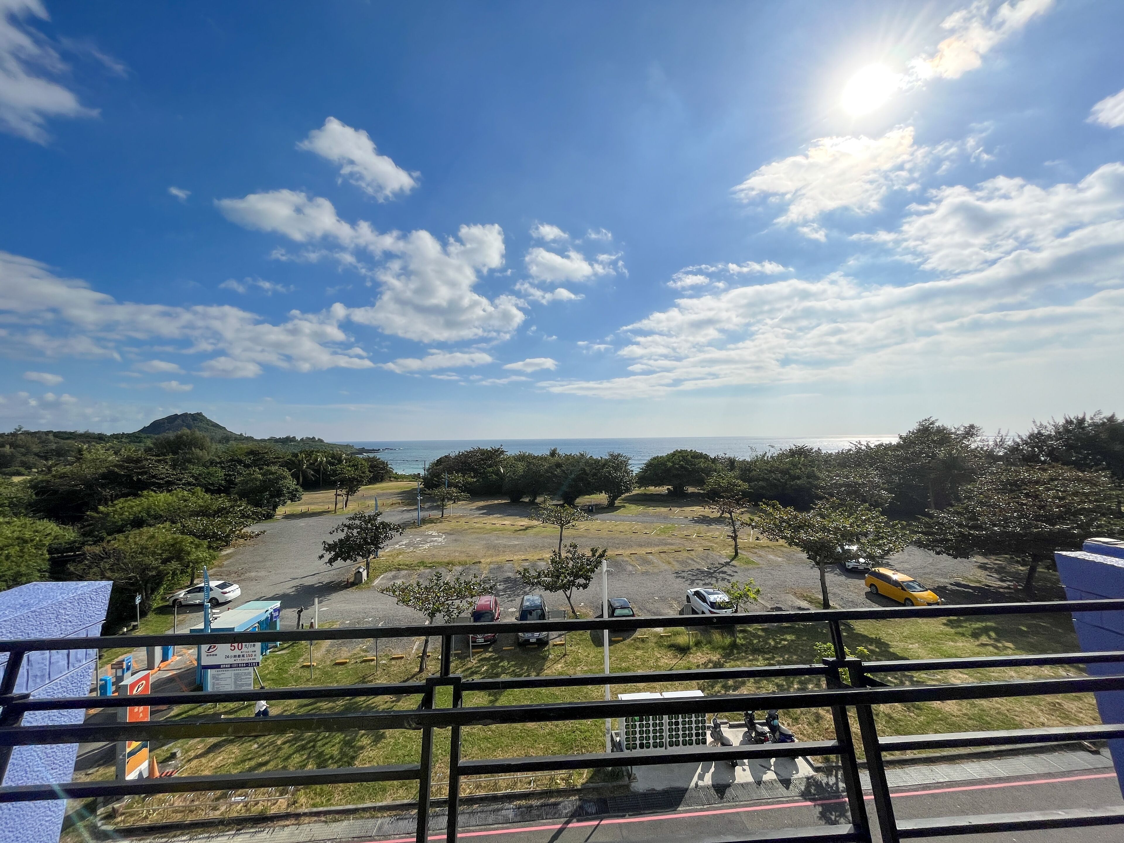 A parking area with vehicles, a clear sky, and a distant view of the sea.