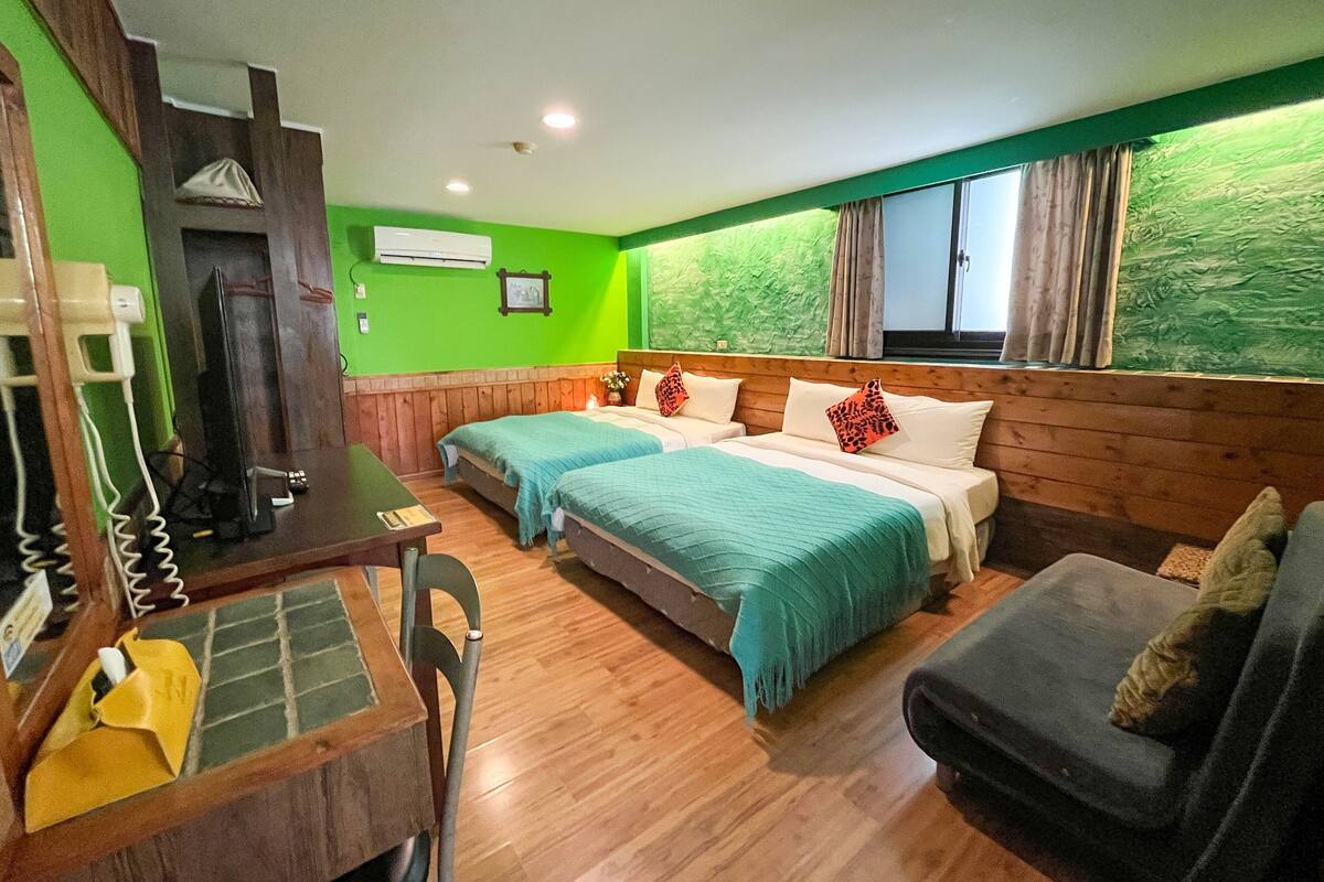 Habitación de hotel con dos camas, un escritorio de madera, una silla, un sofá y una ventana con cortinas.