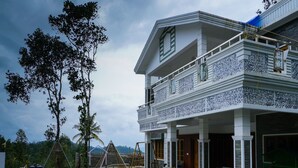A two-story building with a balcony, a tiled entrance, and a view of trees and hills in the background. - OYO 16630 Home Cocoa Tree Residency (Devikolam)