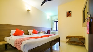 A hotel room with a large bed, a wooden headboard, a bedside table, a small wooden bench, and a ceiling fan. - OYO 3633 Nanda Inn (Kanayannur)