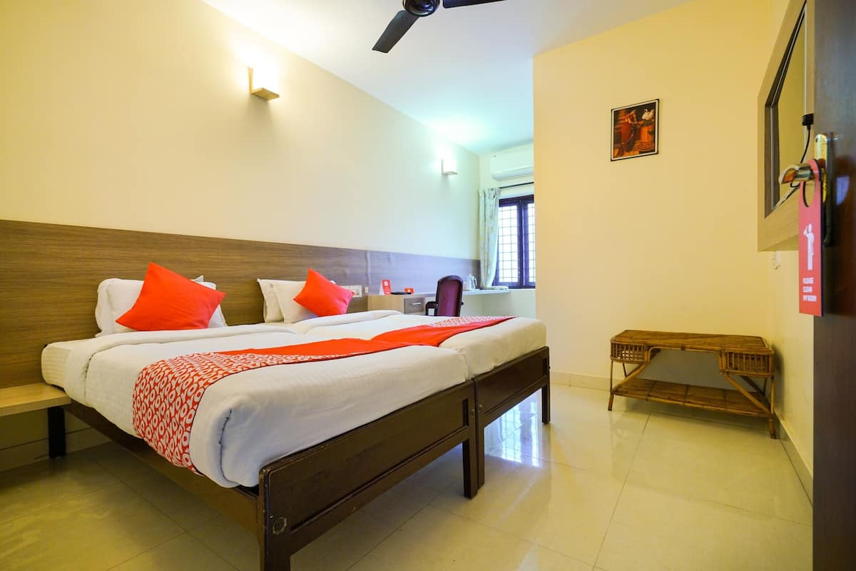 A hotel room with a large bed, a wooden headboard, a bedside table, a small wooden bench, and a ceiling fan.