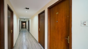 A long, narrow hallway with wooden doors on both sides, leading to a room at the end. - OYO 3633 Nanda Inn (Kanayannur)