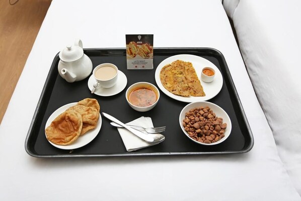 A tray with a teapot, cups, a bowl of soup, a plate of flatbread, a bowl of beans, and a packet of late-night hunger pangs snack.