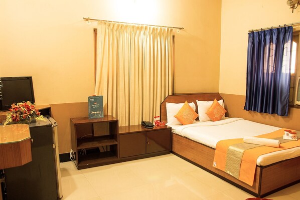 A hotel room with a bed, bedside table, TV, and curtains.