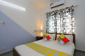 Ein Schlafzimmer mit einem Bett, einem Nachttisch, einer Lampe und einem Fenster mit gemusterten Vorhängen.