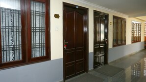 A hallway with three wooden doors, each with a metal grid window. - OYO 23654 Home Cozy 2BHK Aluva Metro Station (Aluva)