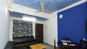A room with a blue wall, a ceiling fan, a black leather sofa, a wooden coffee table, and a dining table with chairs. - OYO 23654 Home Cozy 2BHK Aluva Metro Station (Aluva)