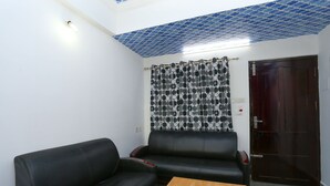 A room with a black leather sofa, a wooden coffee table, and a patterned curtain. - OYO 23654 Home Cozy 2BHK Aluva Metro Station (Aluva)