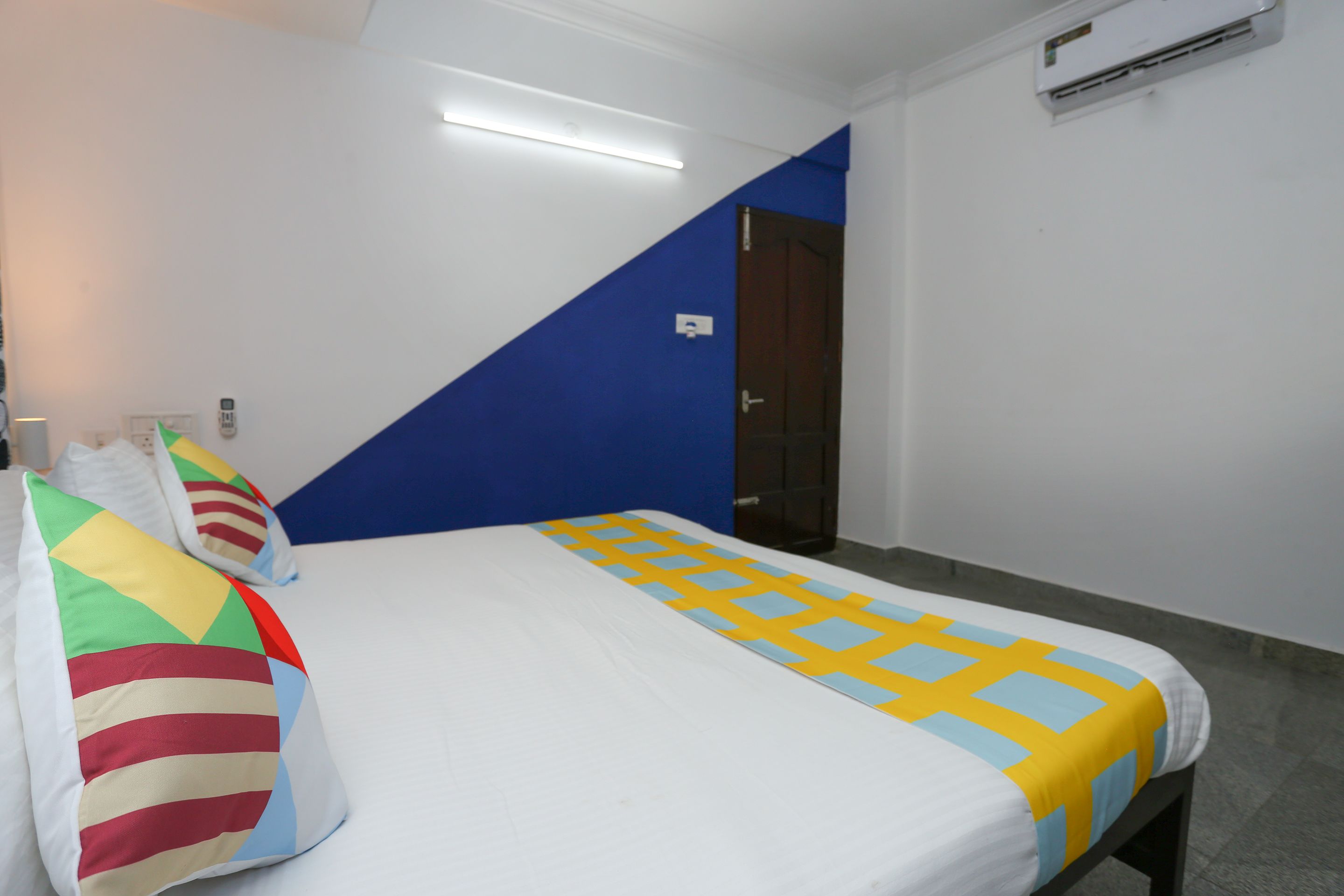 A hotel room with a bed, a blue accent wall, and an air conditioning unit.