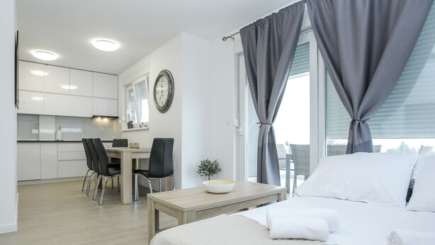 A modern hotel room with a bed, a dining area, and a view of the city. - Apartments Villa Dalia (Novalja)