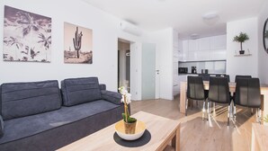 A modern living room with a grey sofa, a wooden coffee table with a plant, and a dining area with a wooden table and chairs. - Apartments Villa Dalia (Novalja)